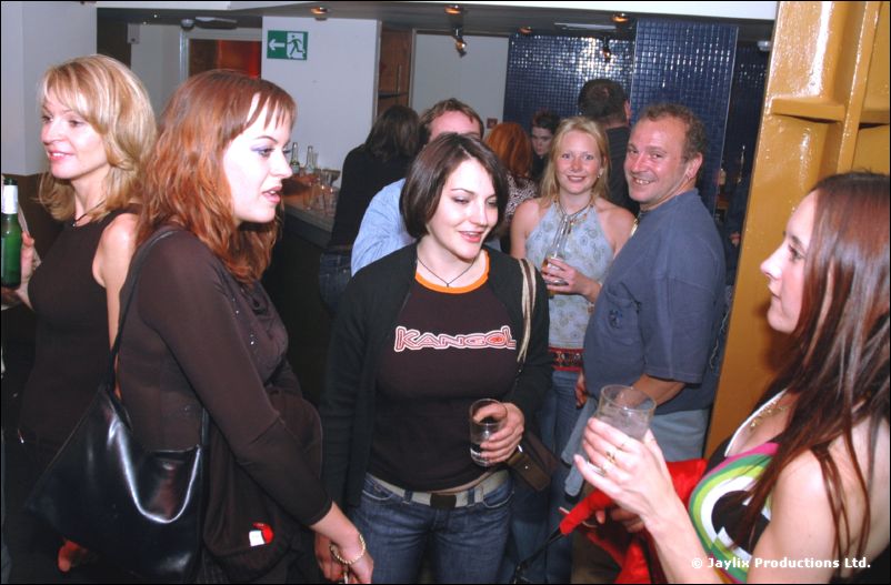 A group of women and men stand chatting with drinks in a busy bar