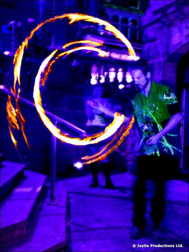 A person in a green shirt spins a ring of fire on stone steps, lit in purple and blue