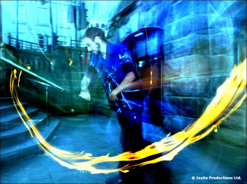A person in dark clothes spins a ring of fire beside stone steps, lit in blue and cyan