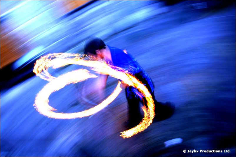 A crouching person spins loops of fire, blurred in blue tones