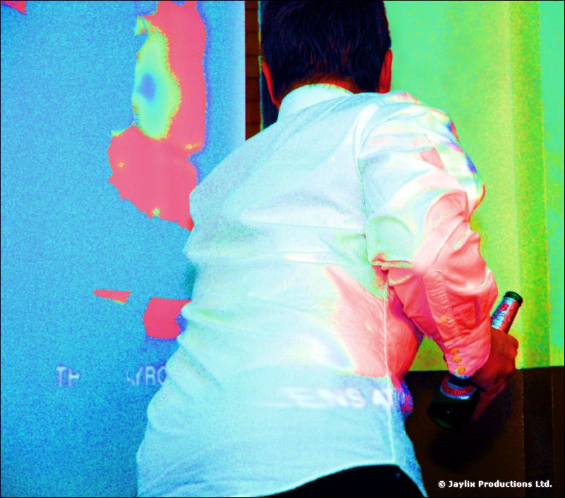A person in a white shirt holding a can stands facing a brightly coloured projection
