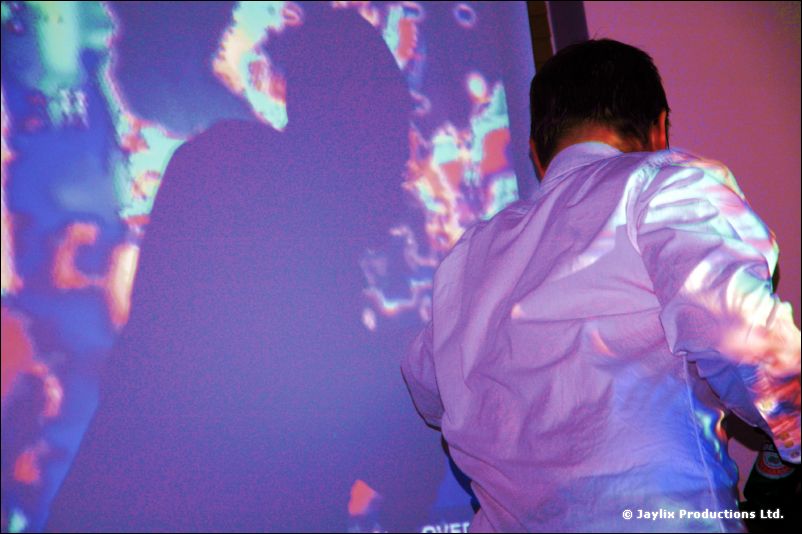 A person in a white shirt stands before a purple and blue projection