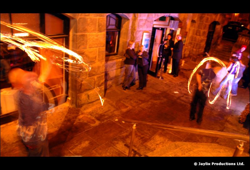 High view of a stone-walled street at night with trails of fire and people standing around