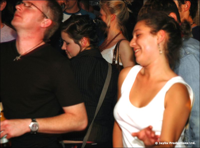 A crowd dancing closely, a man with glasses tilting his head back and a woman in a white top smiling