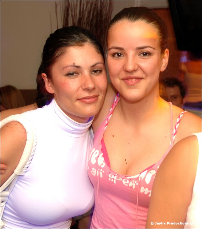 Two women pose cheek to cheek, one in a white turtleneck and one in a pink top
