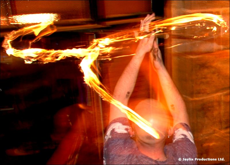 A person with raised hands in front of a bright trail of fire in a dark room