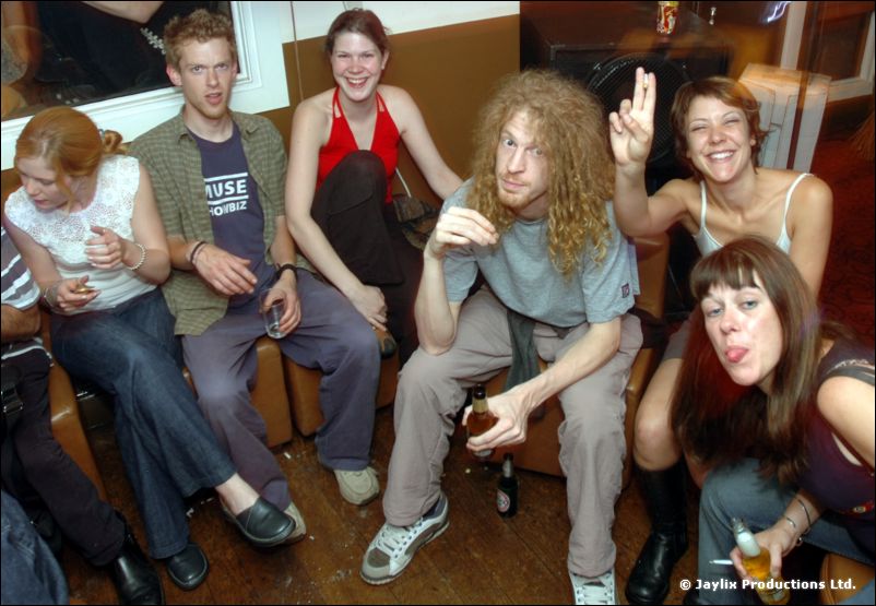 A group sits on a bench seat, some making peace signs and pulling faces, one in a Muse t-shirt