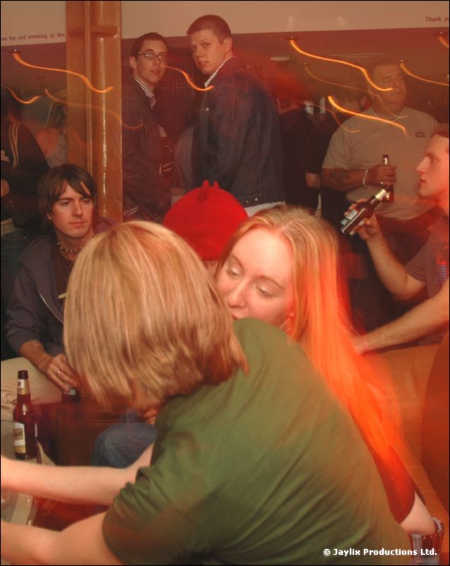Seated people in a bar, with two people embracing in the foreground