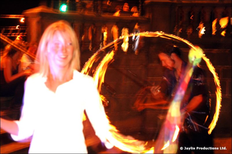 A smiling woman in white with a ring of fire behind her in a dark room