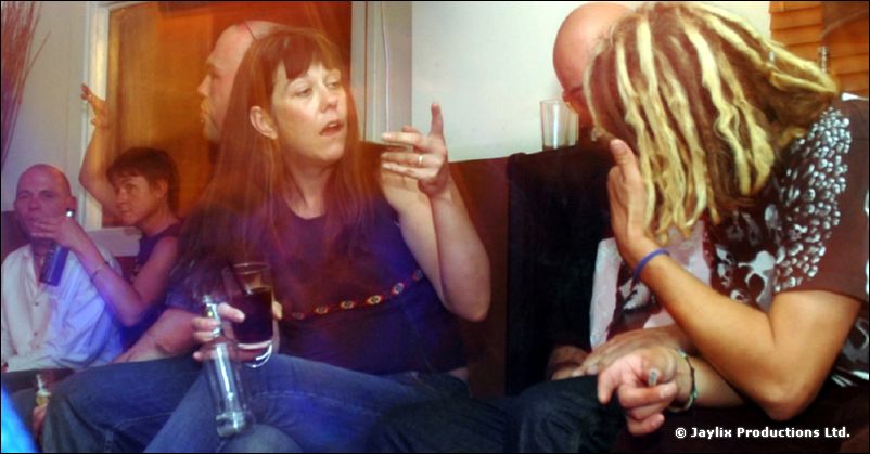 People sit close together on a sofa, a woman in a navy top talking with a person with dreadlocks