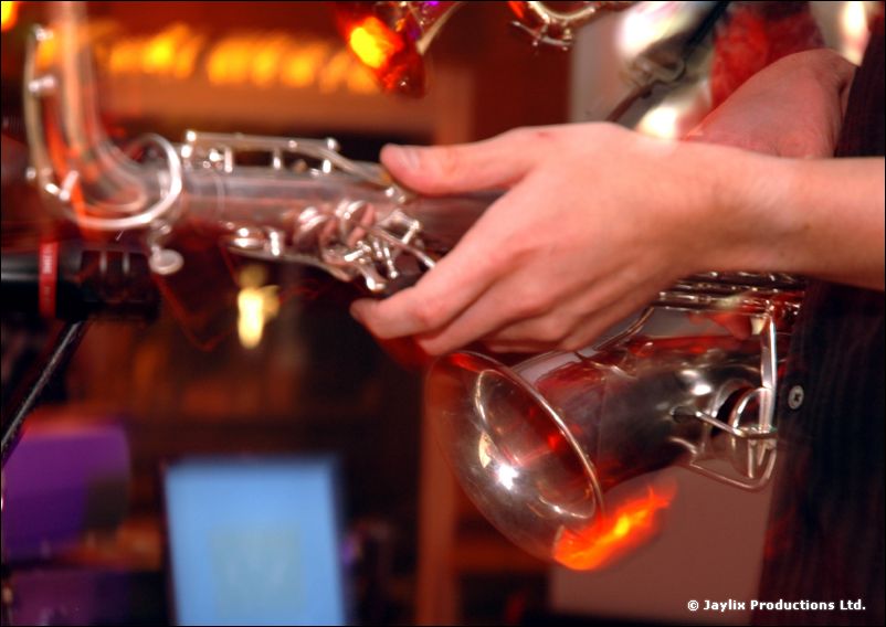 Close view of a hand holding a silver saxophone in an orange-lit bar