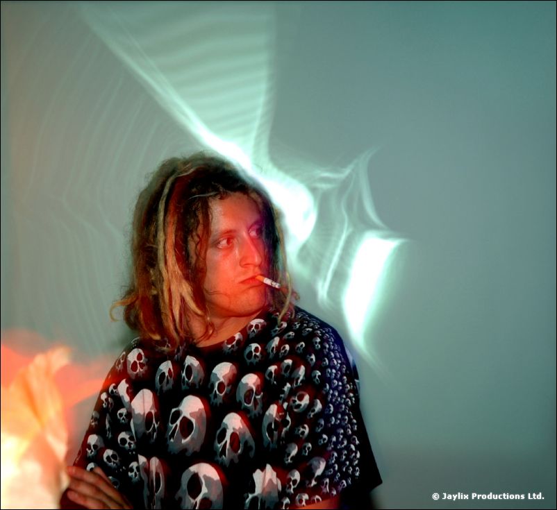 A person with dreadlocks in a skull-print t-shirt smokes in front of a pale green projection