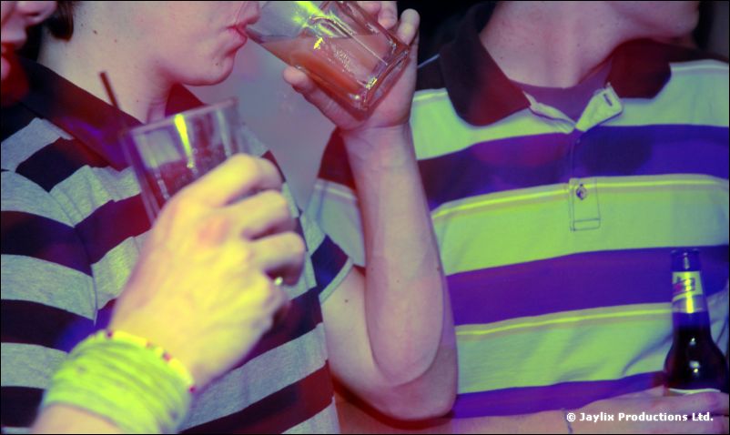 Two people in striped polo shirts drink from glasses, one wearing a green wristband