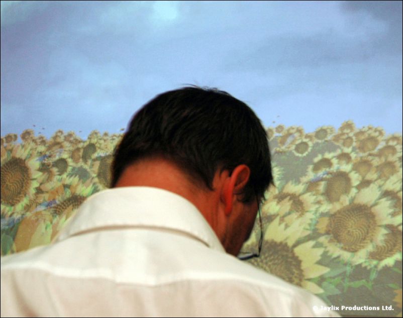 A man in a white shirt seen from behind in front of a projected field of sunflowers