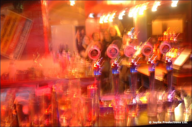 A blurred long exposure of a bar with beer taps and glasses in orange and pink light