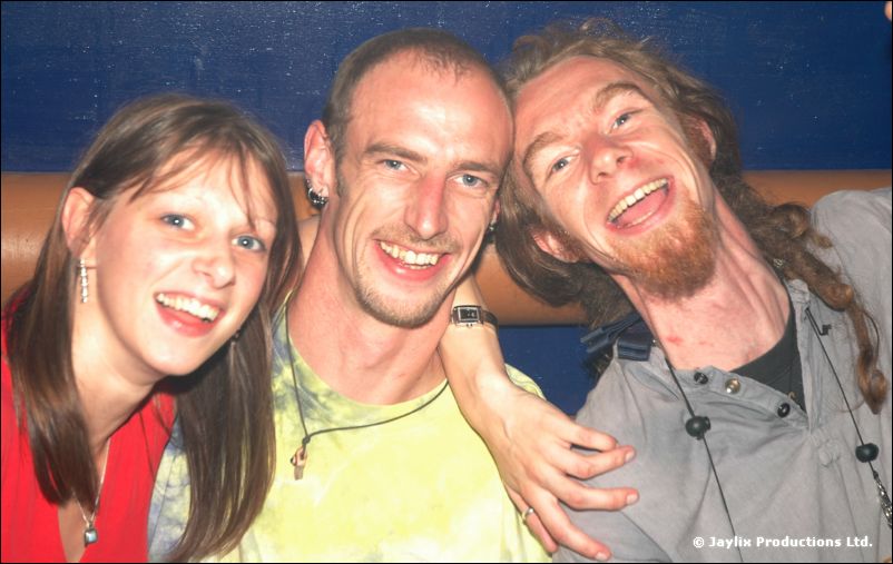 Three people with their arms around each other smiling at the camera against a blue wall