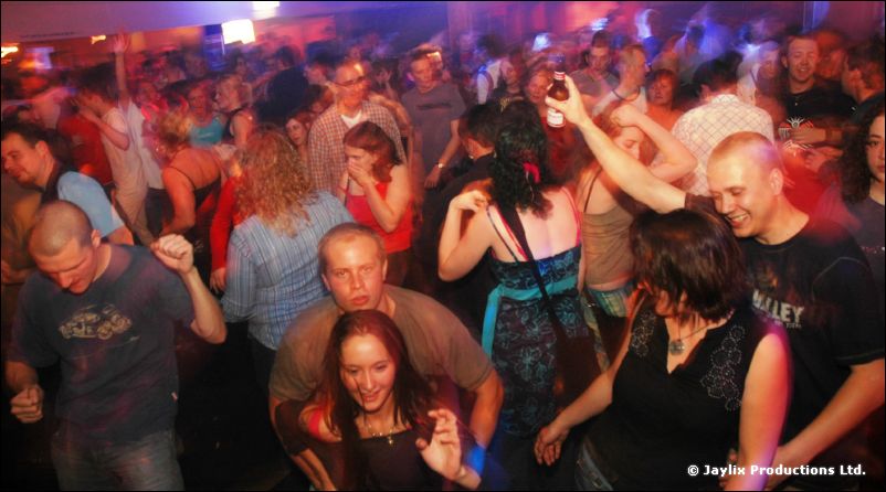 A packed dancefloor of people dancing and looking at the camera
