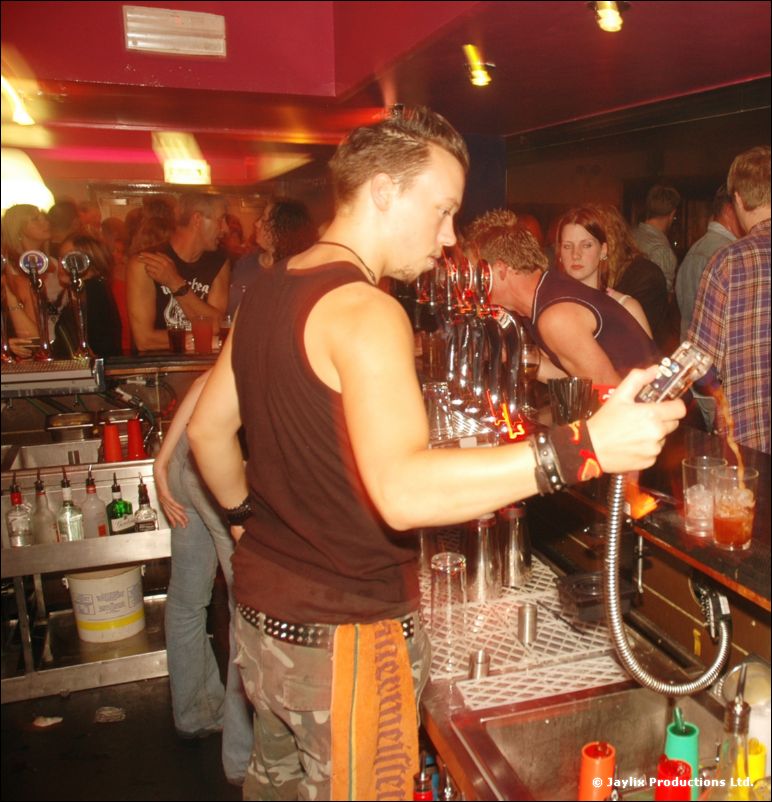 A bartender in a sleeveless top pulls a pint at a busy bar