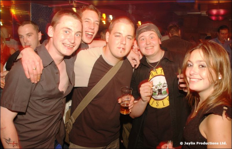 A group of five people smiling at the camera in a bar, one holding a pint