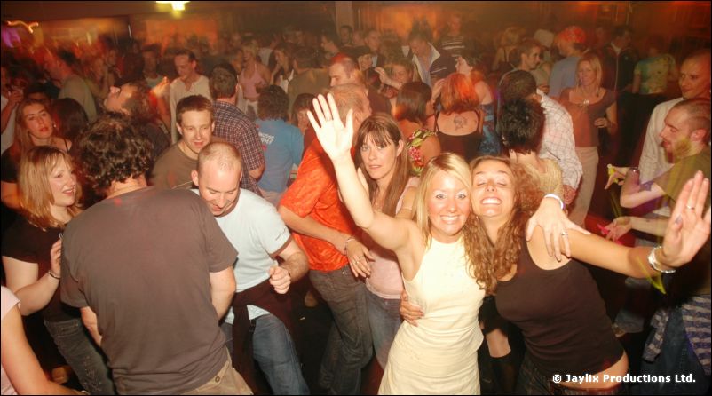 A crowded dancefloor with people dancing, two women in the foreground raising their arms