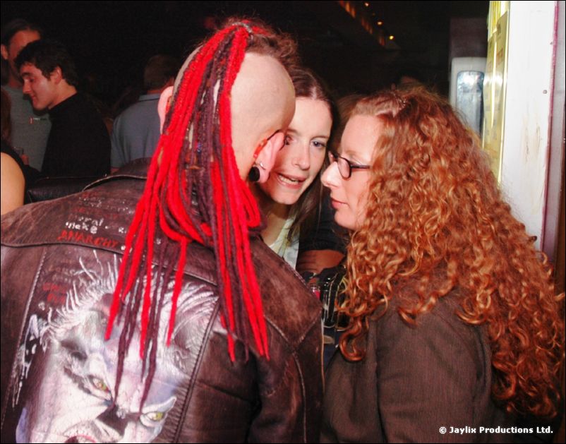 A person with a red dreadlocked mohawk and leather jacket next to a woman with curly red hair and glasses