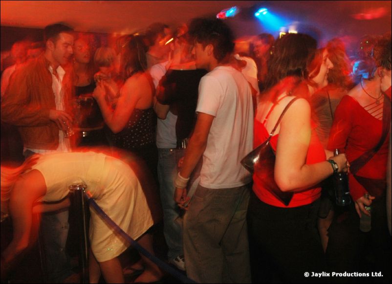 Dancing people in a crowd, one person bent forward beside a rope barrier