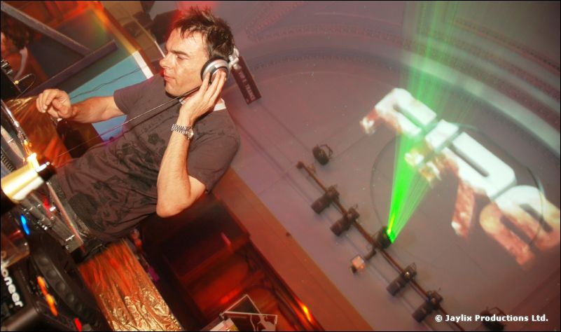 A DJ with headphones at the decks, tilted view, with a green laser and "FIRE" logo behind