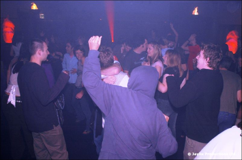 Dancers in a dark room, one wearing a hooded top with a raised arm