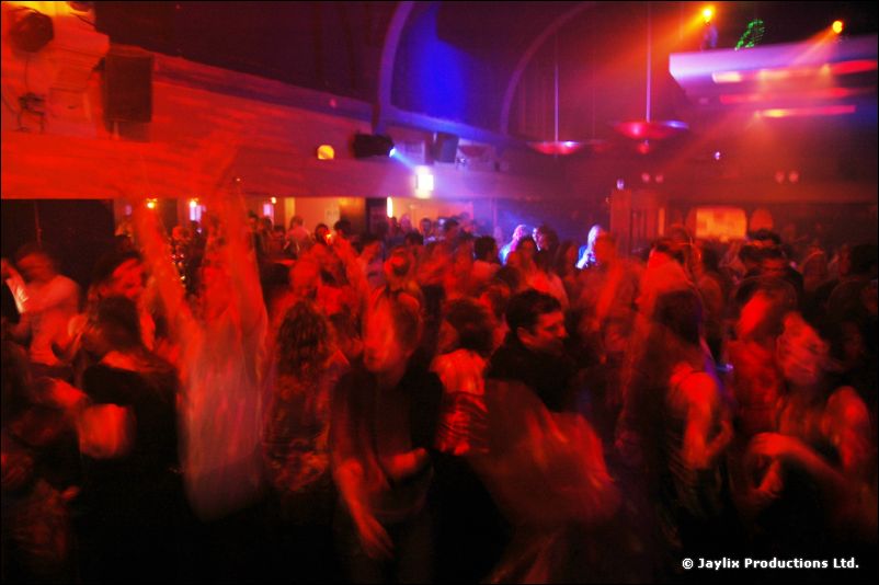 A blurred crowd dancing in a large room lit in red and blue