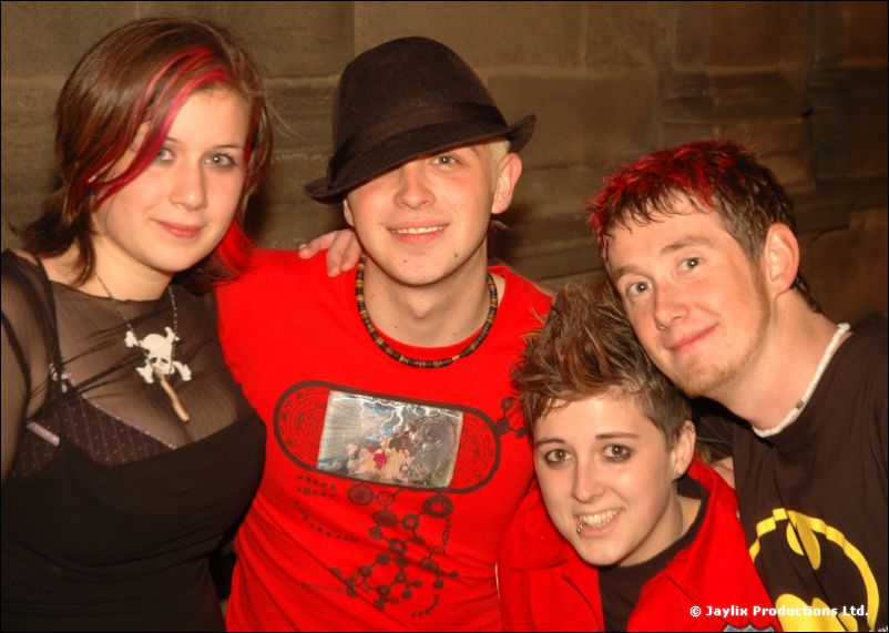 Four people posing together, one in a black hat and red t-shirt, another in a Batman t-shirt