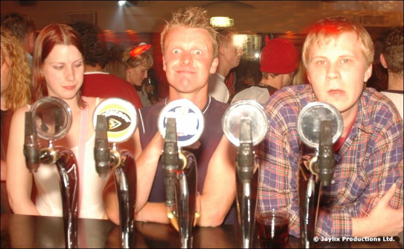Four people lean on a bar behind beer taps, looking at the camera