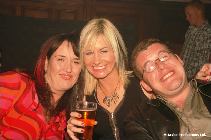 Two women and a man with glasses posing together, one woman holding a pint