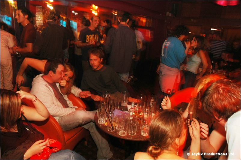 Groups of people sitting around tables with glasses in a busy, dimly lit bar