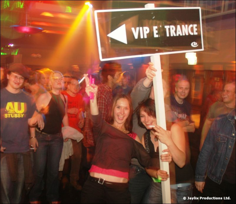 People in a crowd hold up a sign reading "VIP E TRANCE" with an arrow