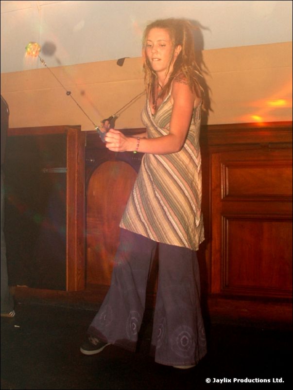 A woman with dreadlocks in a striped dress and flared trousers swings a prop on strings