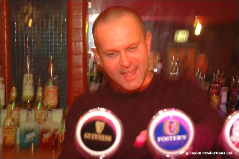 A man leans on a bar behind Guinness and Foster's taps