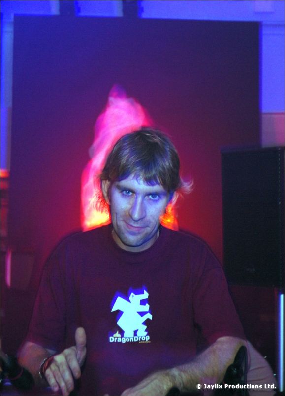 A person in a dark DragonDrop t-shirt with a dragon logo, with a pink glowing shape behind, in blue light