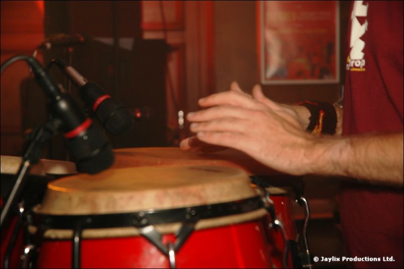 A hand beats a red conga drum with microphones pointed at it