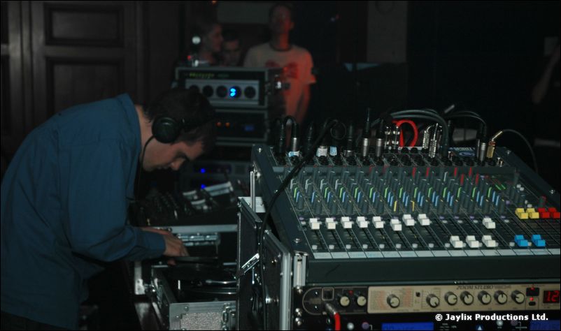 A man in headphones leans over a mixing desk and audio equipment