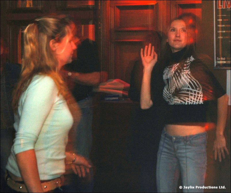 Two women dancing in a bar, one in a pale top and one in a patterned black top