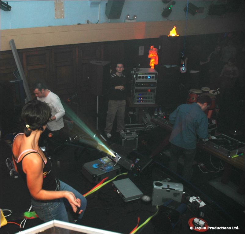 A dark room with a DJ setup, projectors and lights, with a woman dancing in the foreground