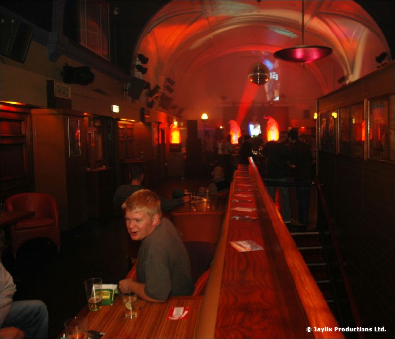 A long wooden bar in a vaulted room with a man seated at a table in the foreground