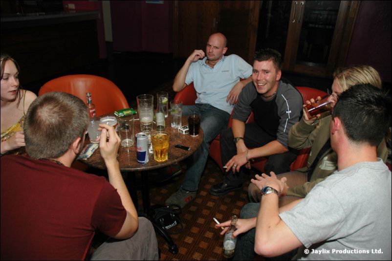 Five people sit around a small table with drinks and cans in a bar