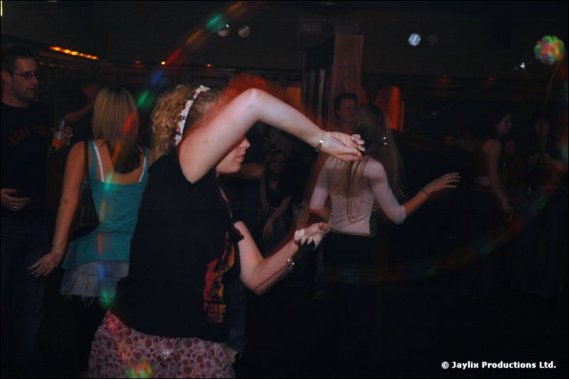 A woman dances with her arm raised in a dim room, with other dancers behind