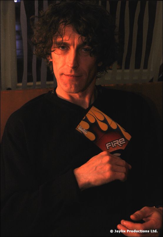 A dark-haired man holds a FIRE flyer against his chest and looks at the camera