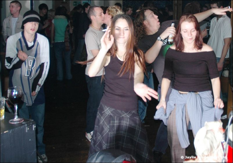 People dance in a crowded bar, two women in dark tops in the foreground
