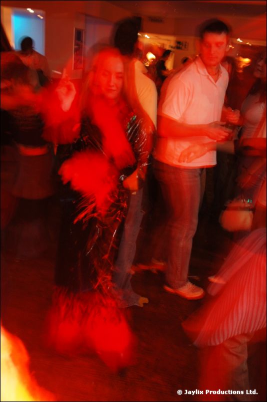 Blurred dancers in a red-lit bar, a woman in black with a red fur trim in the centre
