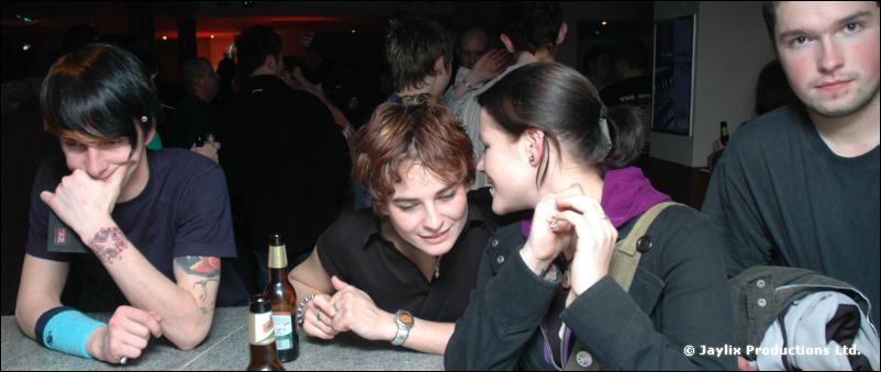 Four people sit at a bar counter, one laughing with head down, bottles in front