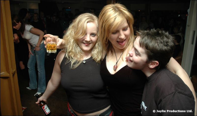 Two women and a young person with dark hair embrace and smile, one holding a drink