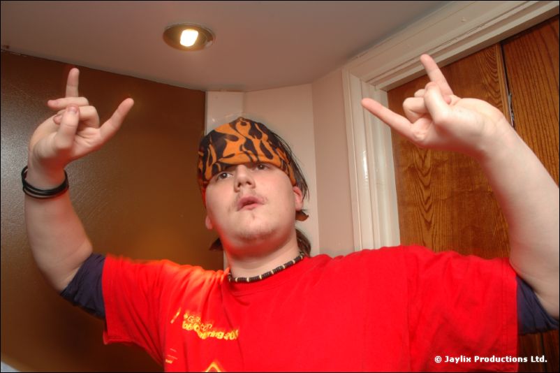 A person in a red T-shirt and patterned bandana holds up both hands in the rock sign